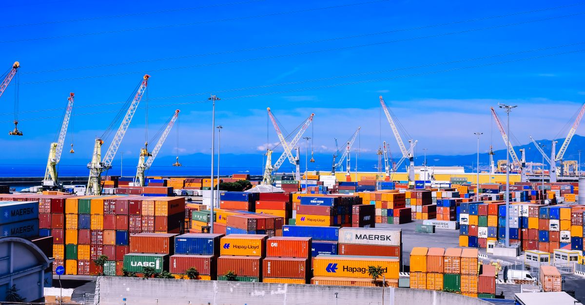 A bustling shipping port with colorful stacked containers and numerous cranes under a clear blue sky.